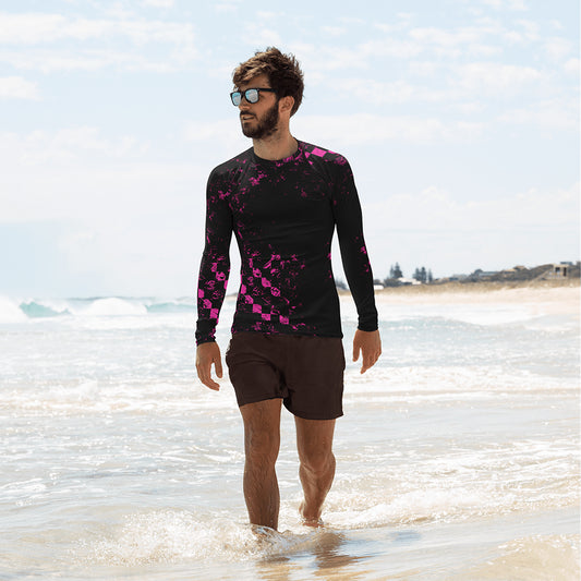 Ein Mann trägt ein Rashguard mit dem Motiv Abstract Squares. Er ist am Strand und läuft durch das flache Wasser. Dabei schaut er auf das Meer hinaus.